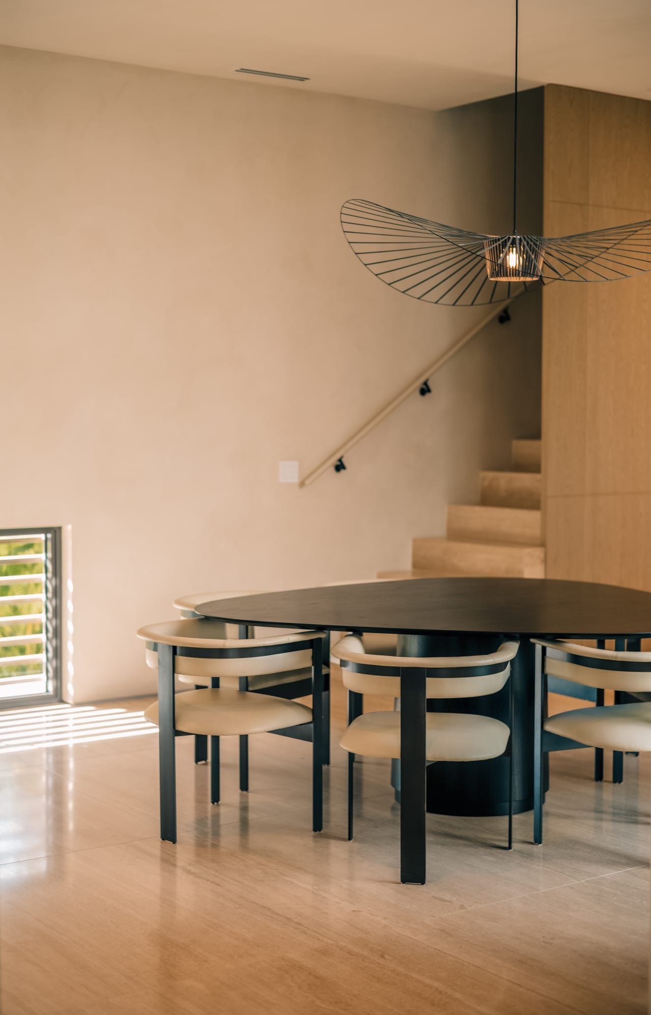 Dining room with a round table, sculptural pendant, and a travertine stair beyond