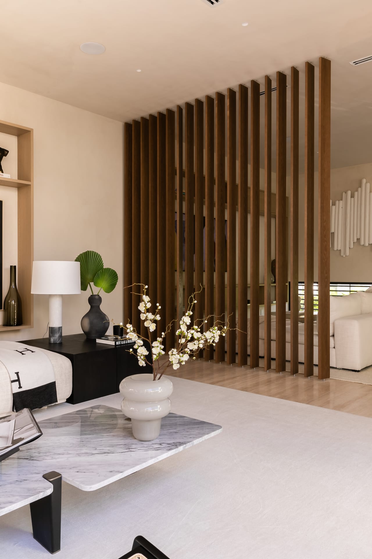 Vertical oak slat screen dividing the living space, with a lamp vignette