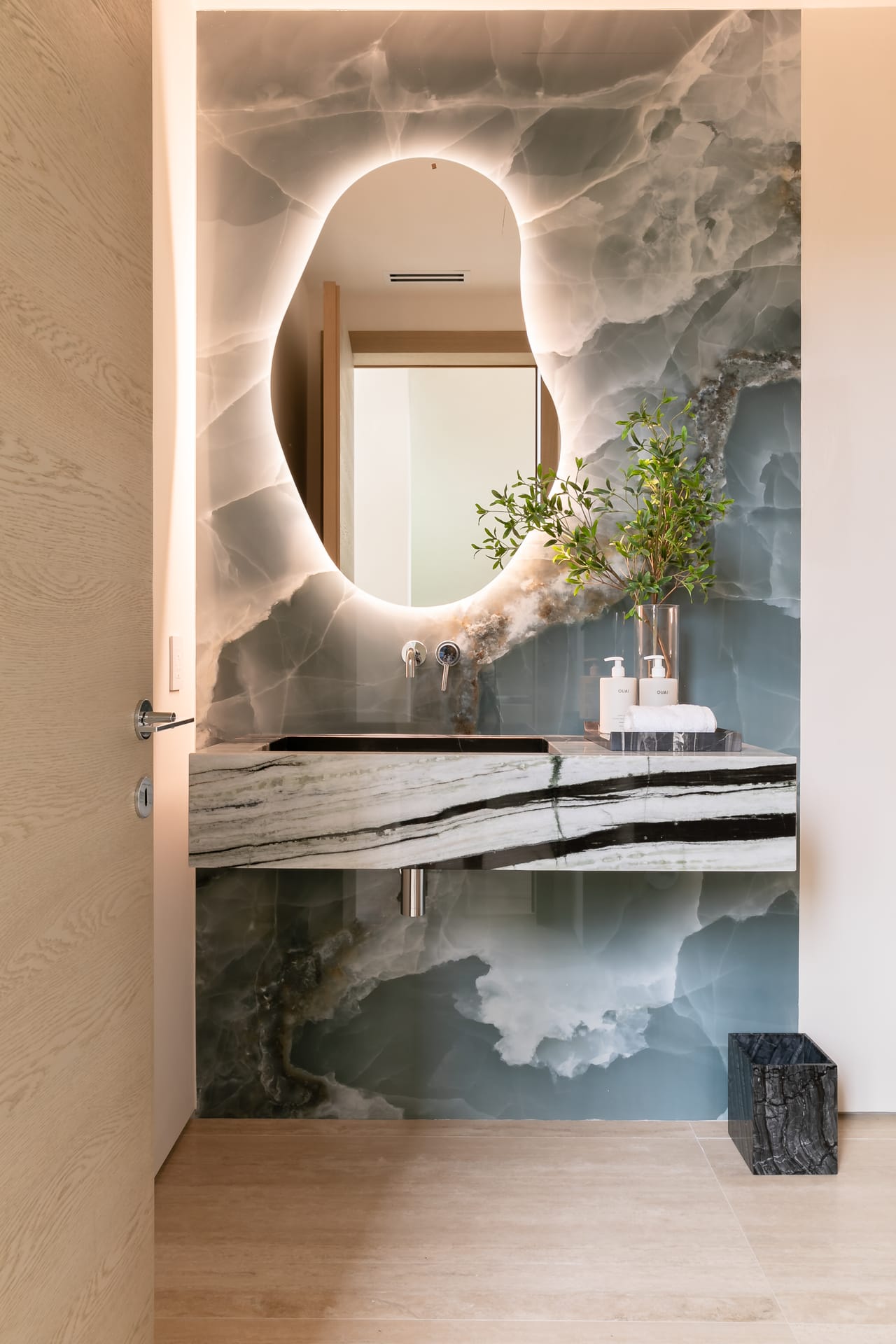 Powder room with a back-lit onyx wall and an organic mirror