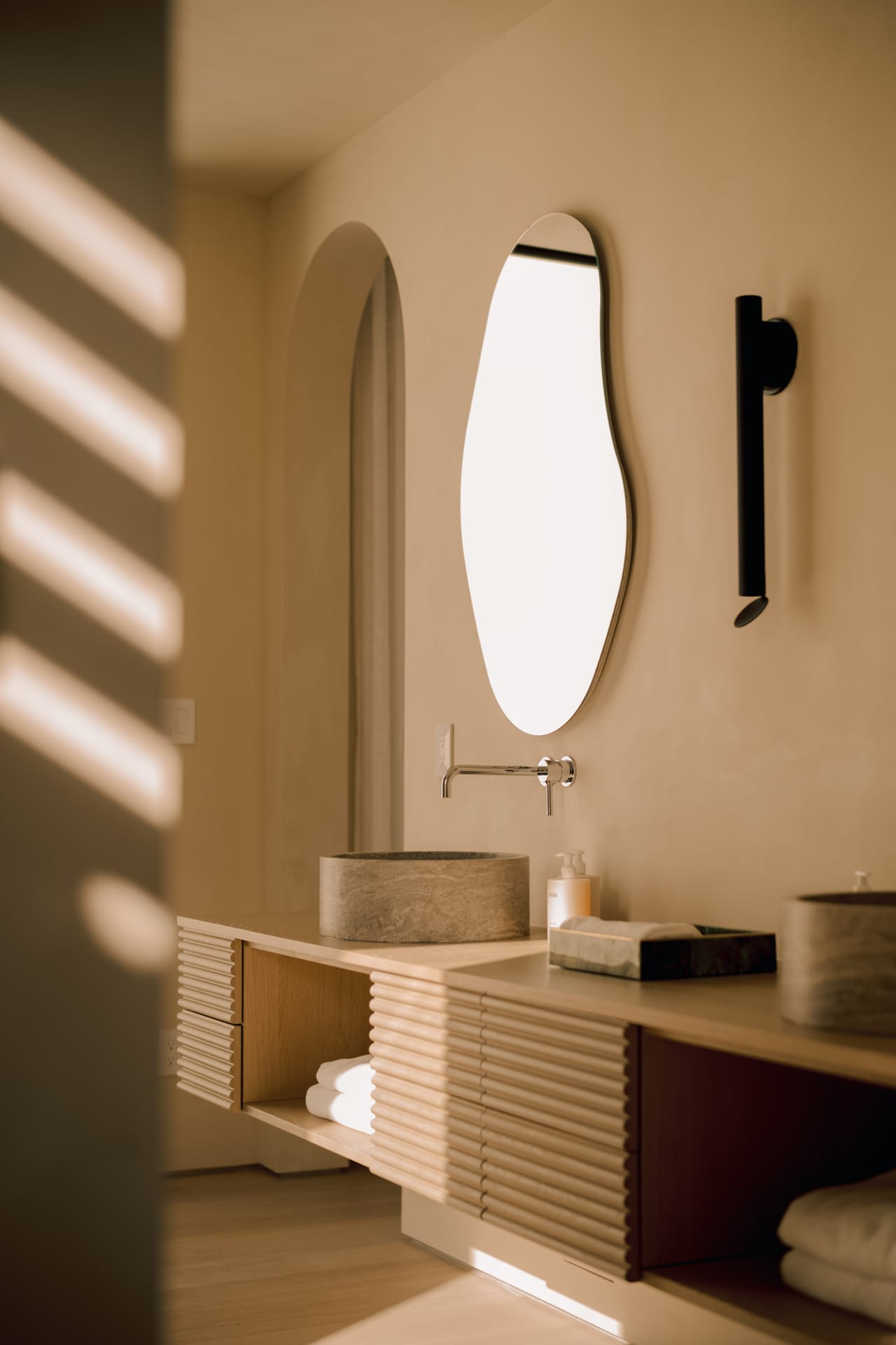 Bathroom with an arched niche, a reeded oak vanity, and a stone basin in striped light