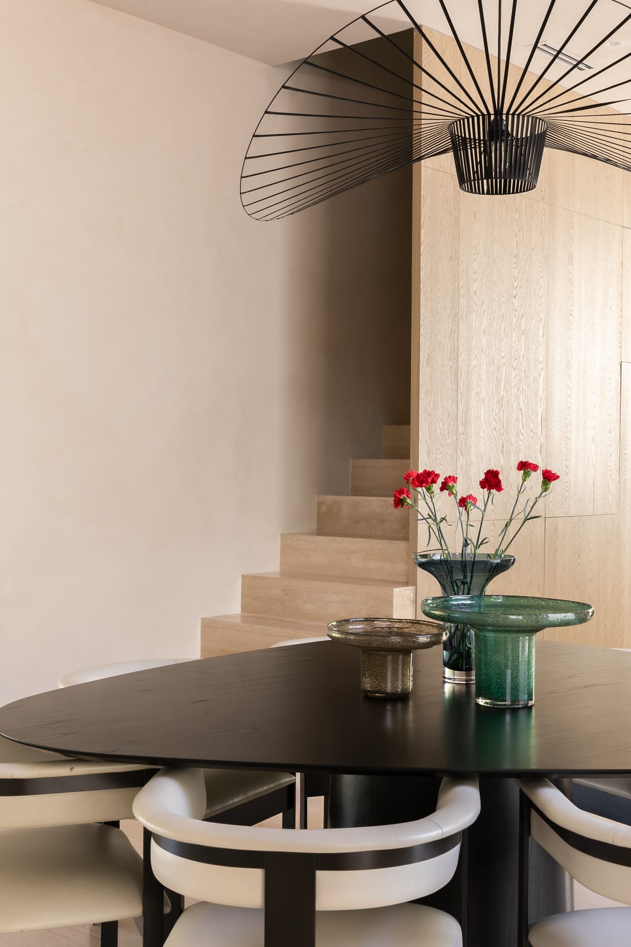 Dining table beneath a sculptural stair and pendant, with flowers