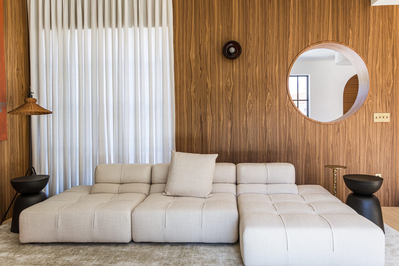 Living room clad in walnut boiserie with a circular porthole window and floor-to-ceiling curtains