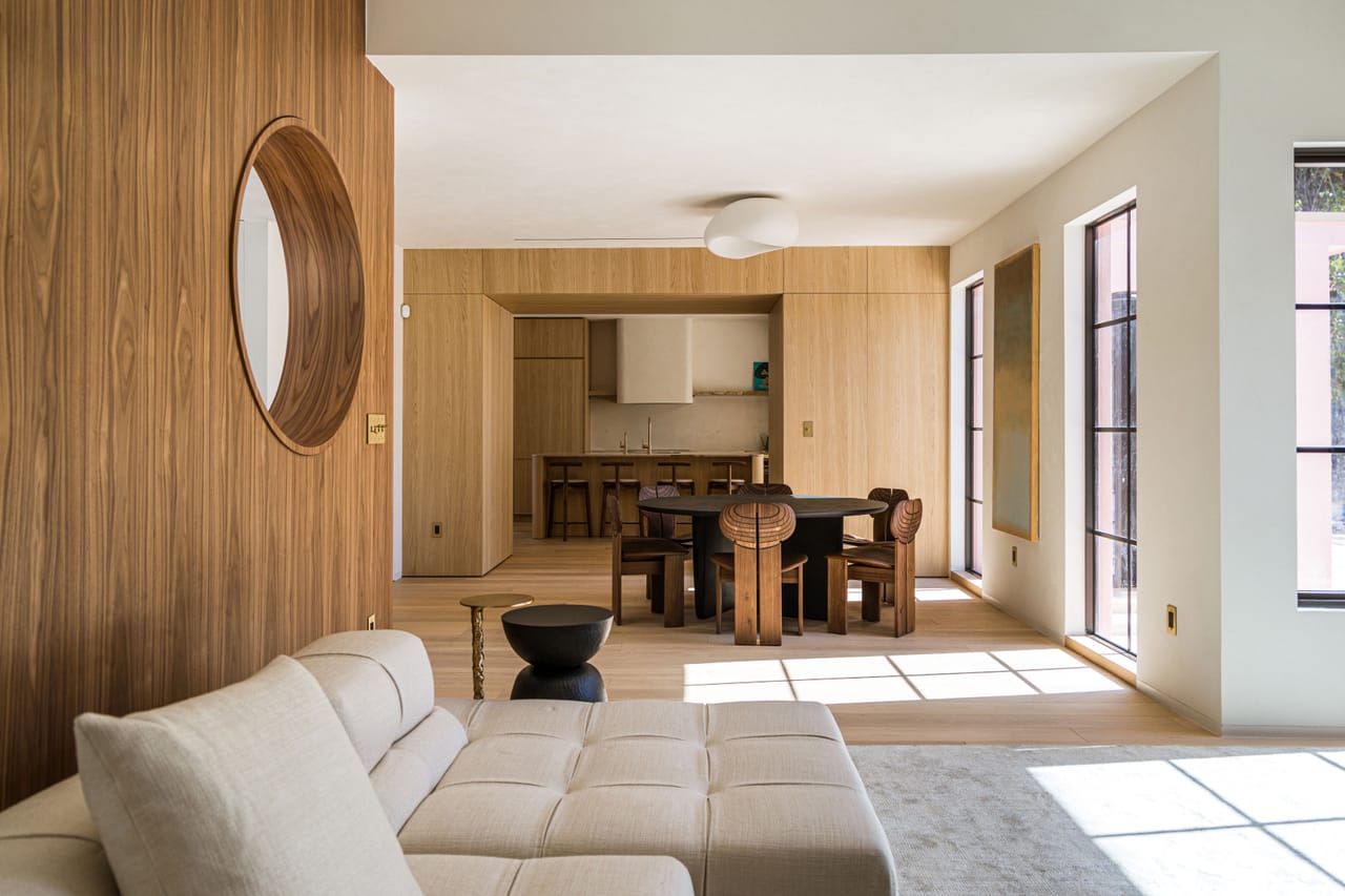 Walnut-panelled living room with a round porthole window, curved wall, and a cream sectional in raking light