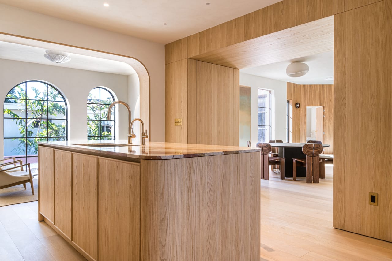 Waterfall oak island beneath arched steel windows in an open-plan kitchen