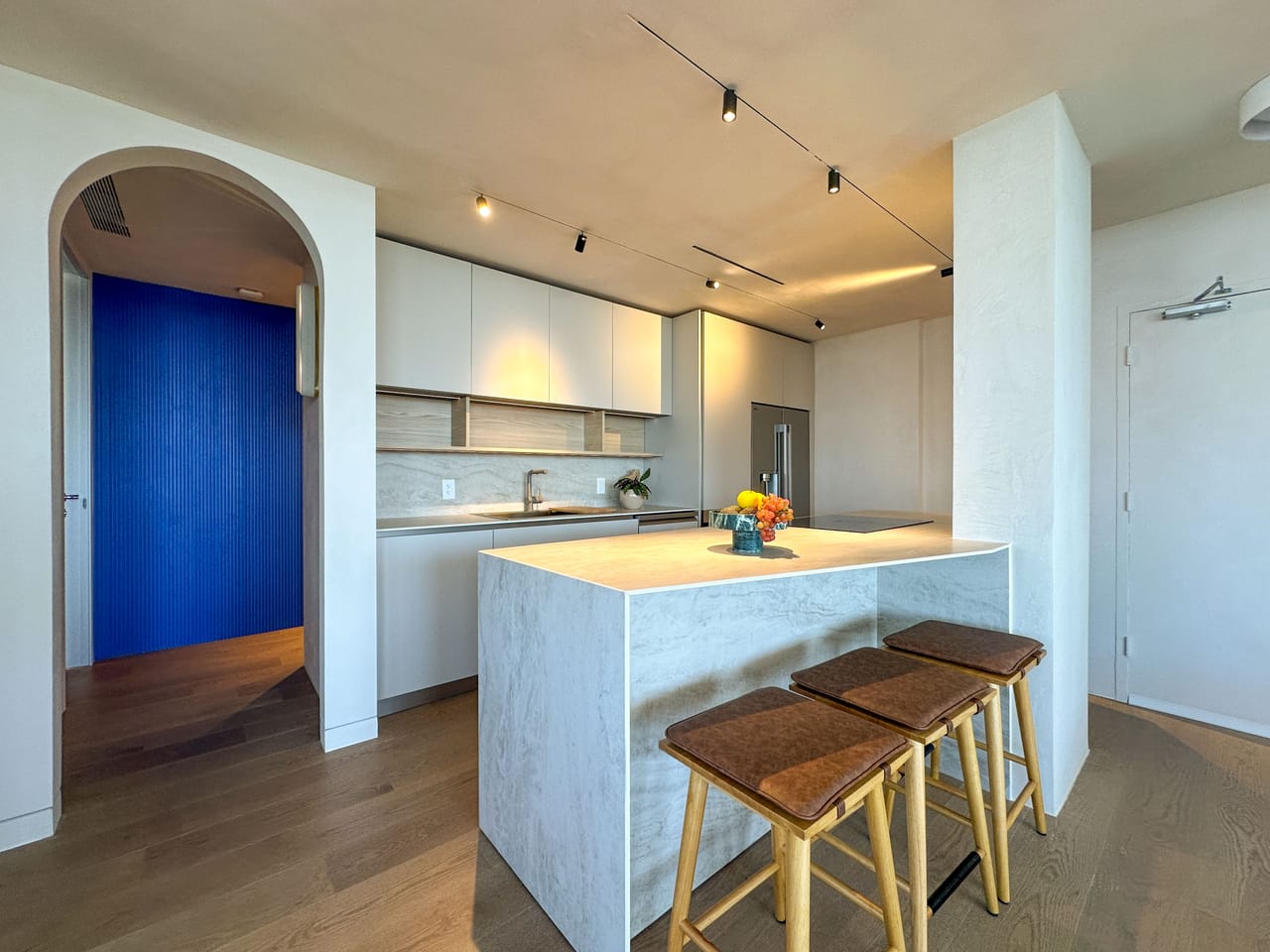 White kitchen with a travertine waterfall island and cork stools